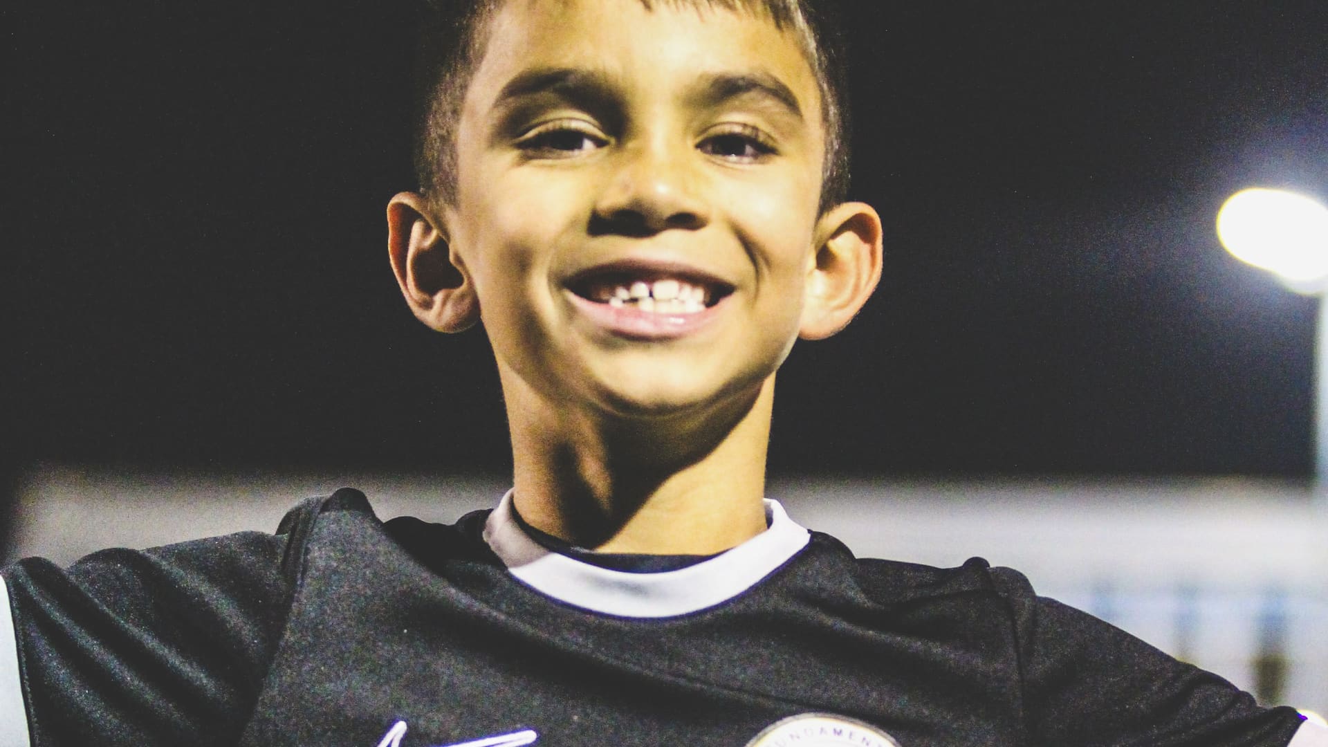 A Fundamental FC player smiling in club kit under the floodlights